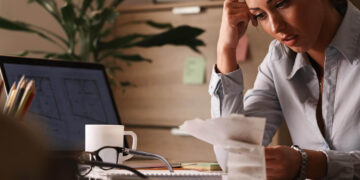 Mulher concentrada em documentos financeiros, destacando a necessidade de planejamento para uma reserva de emergência.