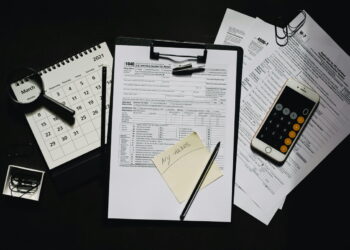 Documentos fiscais usados para cálculos de imposto. Há um celular com calculadora aberta, uma lupa e mais alguns outros elementos na imagem. Falando sobre o revar.